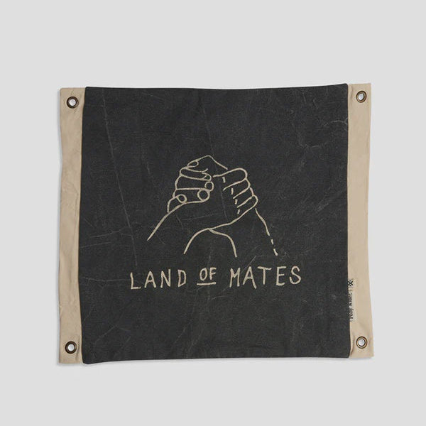 Black fabric banner with a white graphic of two hands holding a bottle and the text 'LAND OF MATES' on a light gray background.
