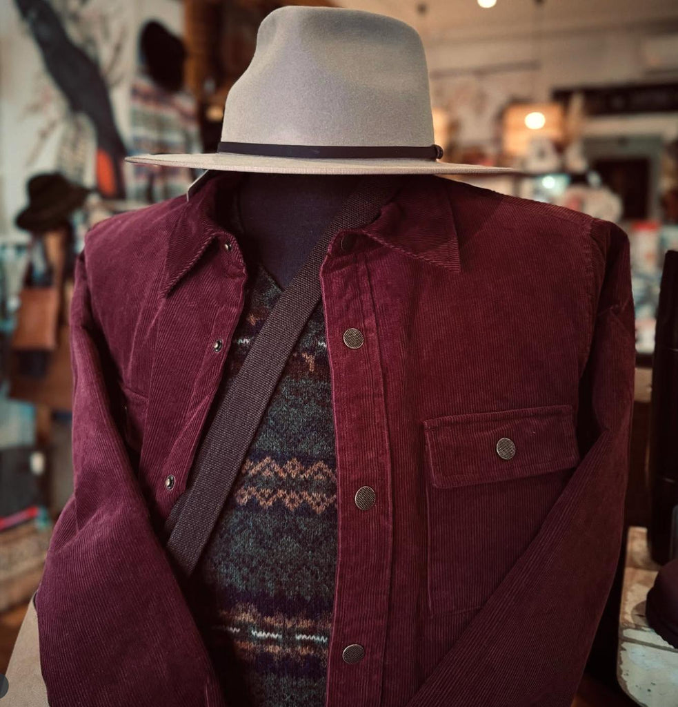Mannequin wearing a maroon jacket, patterned sweater, and beige fedora in a store setting.
