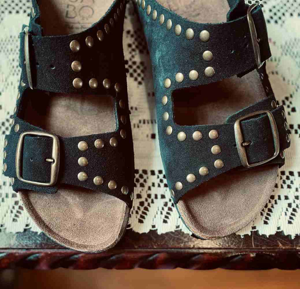 Pair of black sandals with bronze studs on a suede surface