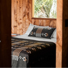 Bed with patterned blanket and pillow in a wooden room with a window showing greenery