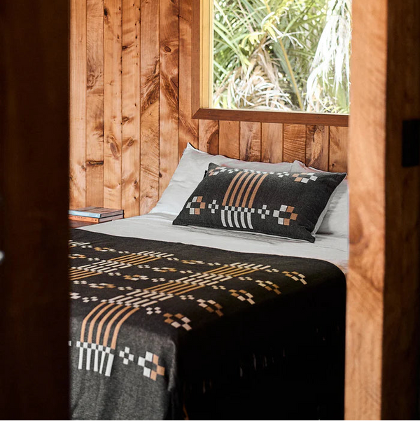 Bed with patterned blanket and pillow in a wooden room with a window showing greenery