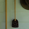 Leather fly swat hanging on a hook against a wooden wall.