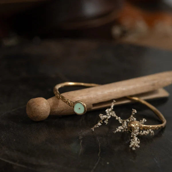 Gold bracelet with a mint resin circle on a wooden stick, with a blurred background