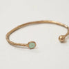 Bronze Pesci Che Volano bracelet with a small round green gemstone on a light gray background