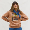 Woman wearing a brown Binny sweatshirt with a cute graphic design and blue scarf against a white background