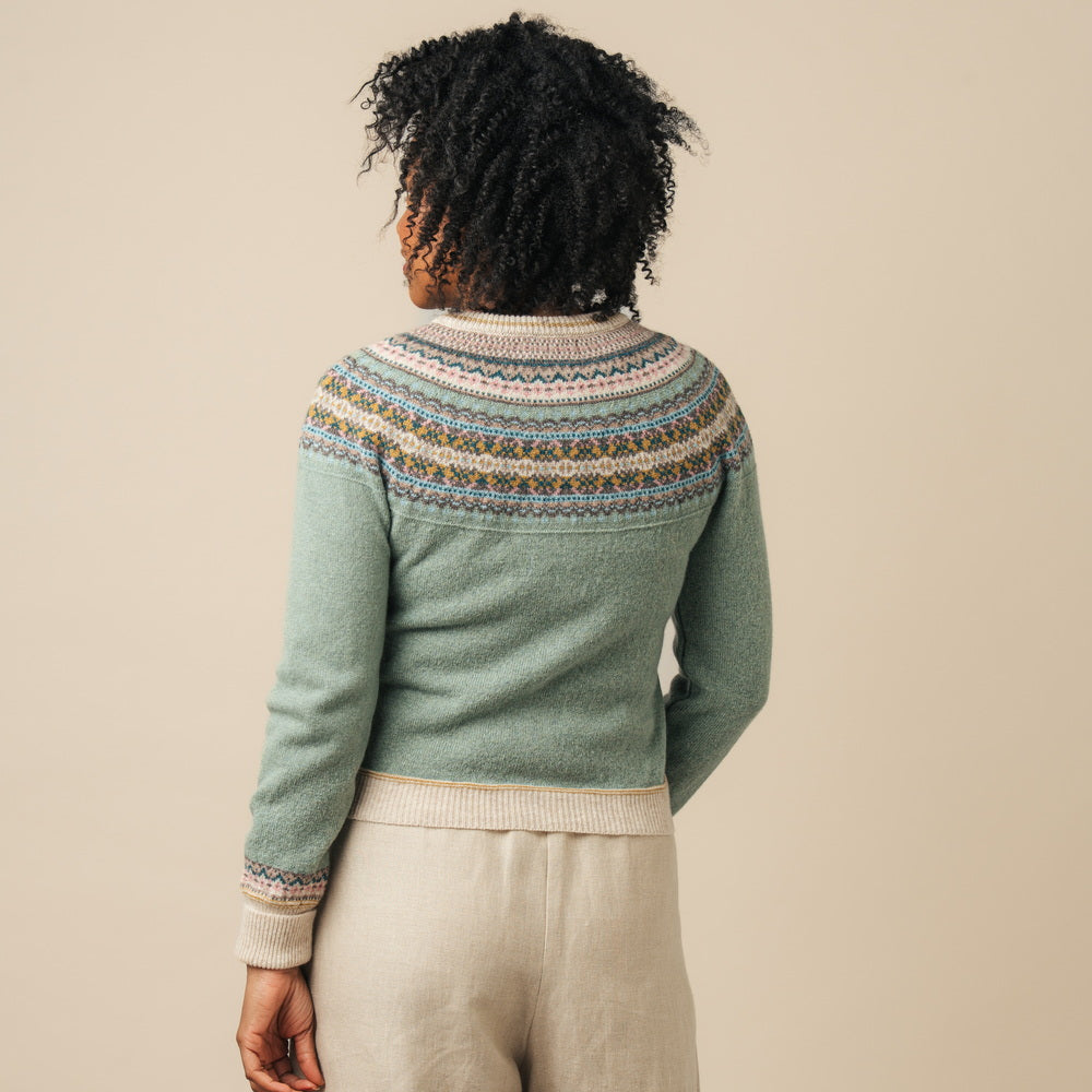 Person wearing a green knitted Eribe cardigan with a patterned yoke against a beige background