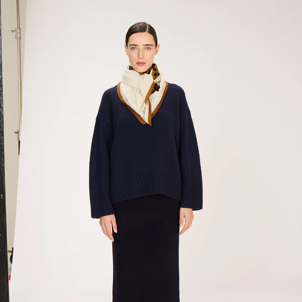 Person wearing a navy sweater with a cream inoui editions scarf and a long black skirt on a white background