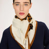 Woman wearing a navy sweater and a cream scarf with brown border, on a white background