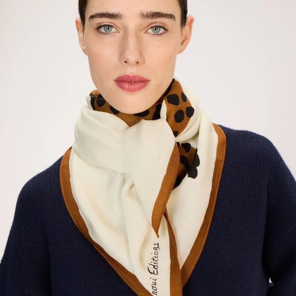 Woman wearing a navy sweater and a cream scarf with brown border, on a white background