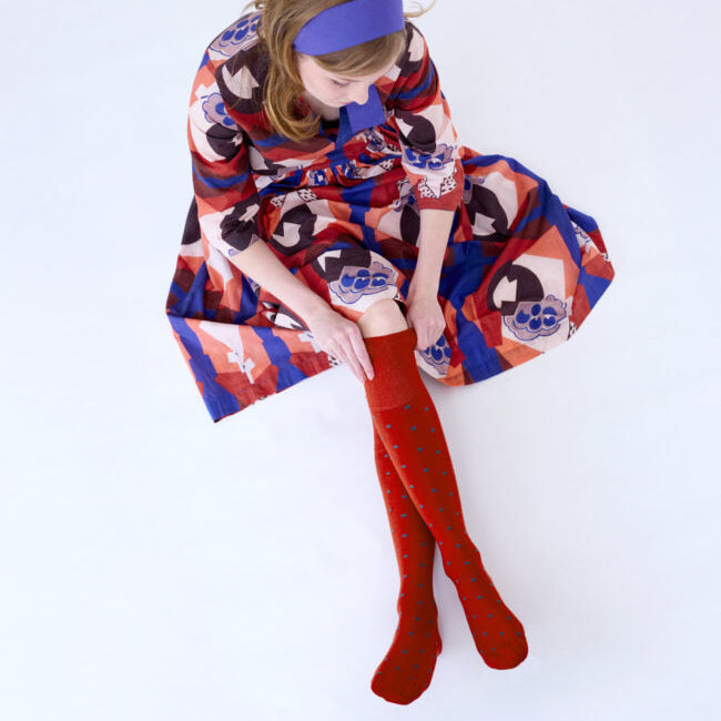 Woman wearing a colorful dress and red knee-high socks sitting on a white background