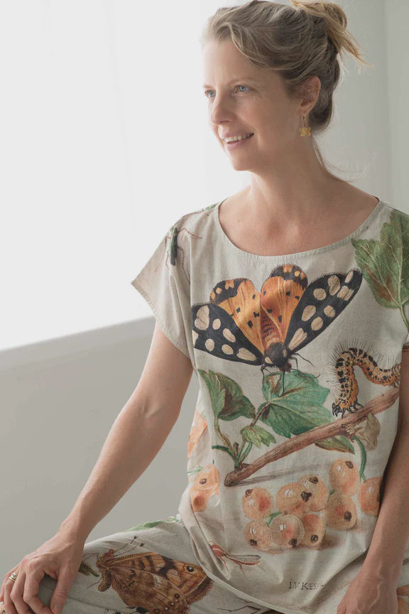 Woman wearing a shirt with butterfly design sitting against a white wall