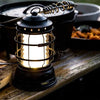 Black lantern on a wooden table with food and camping gear in the background