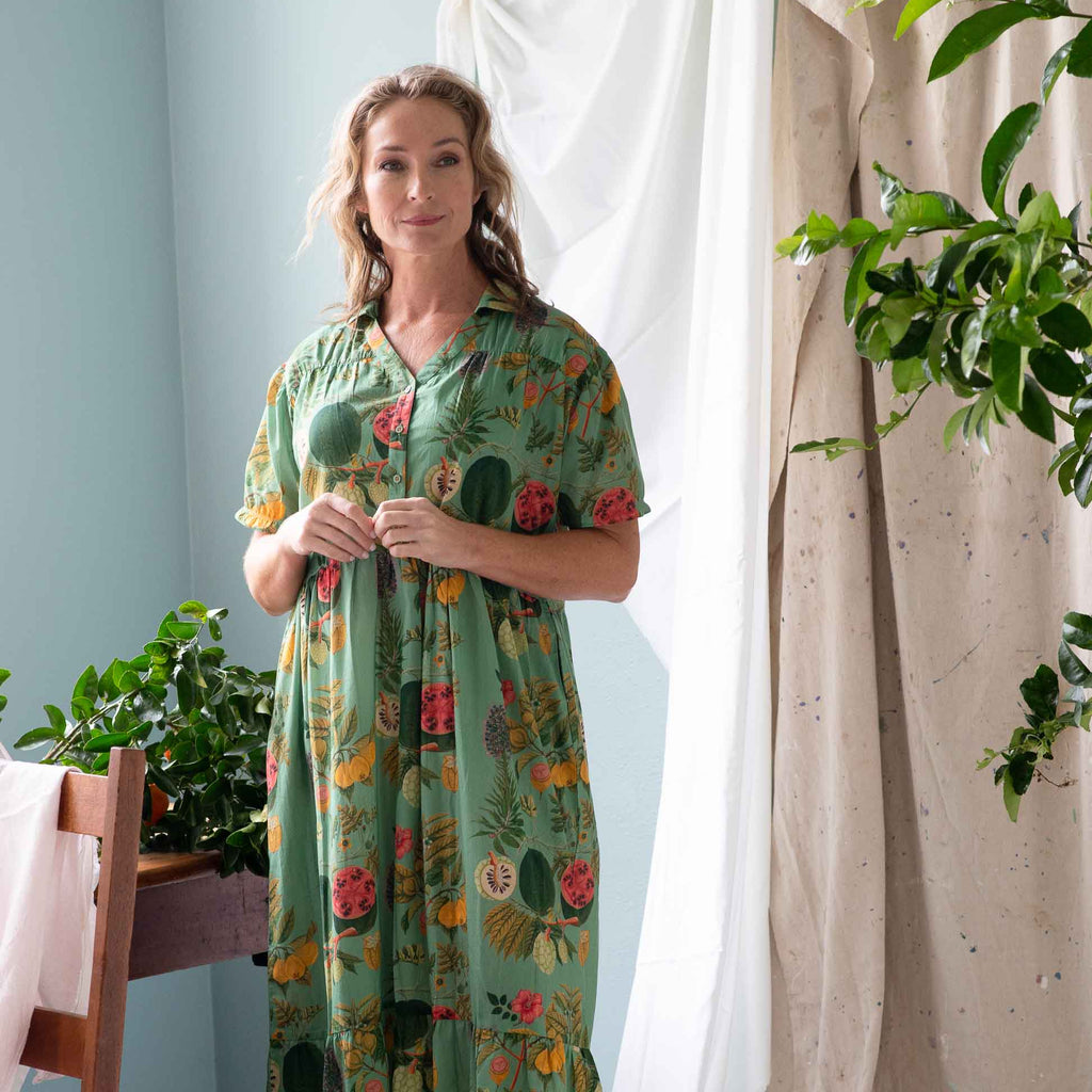 Woman wearing a green floral dress standing in a room with light blue walls and white curtains.