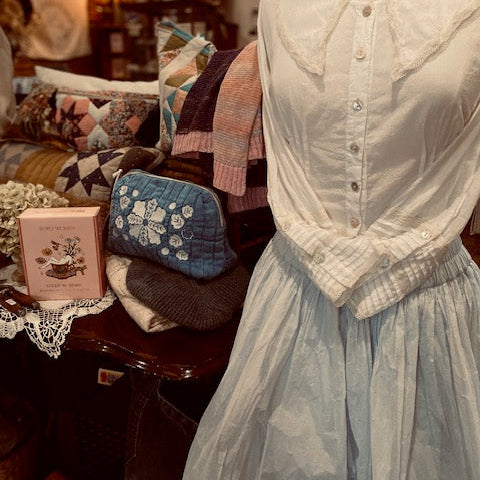 Mannequin wearing a vintage-style dress with a hat in a cozy interior setting.