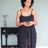 Woman wearing a dark blue slip dress with floral embroidery in a minimal indoor setting.