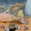 Decorative pillow with a landscape design on a floral-patterned surface with a cup of coffee.