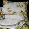 Floral-patterned pillow on a white bed with green bedding against a black background