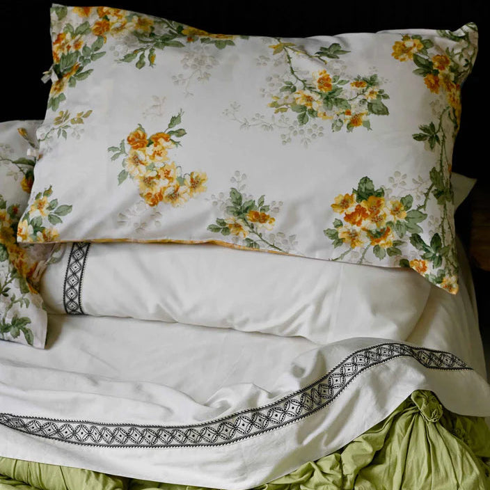 Floral-patterned pillow on a white bed with green bedding against a black background