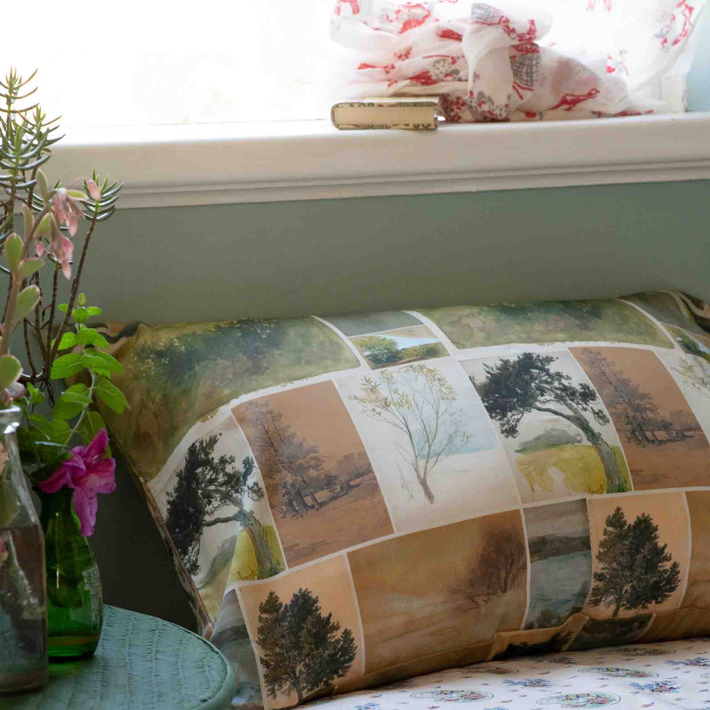 Decorative pillow with nature-themed pattern on a bed next to a window with floral curtains.