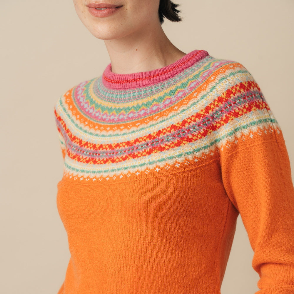 Orange Eribe sweater with colorful patterned sleeves worn by a person on a beige background