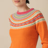 Orange Eribe sweater with colorful patterned sleeves worn by a person on a beige background