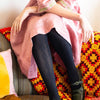 Person wearing black tights sitting on a colorful couch with a pink garment.