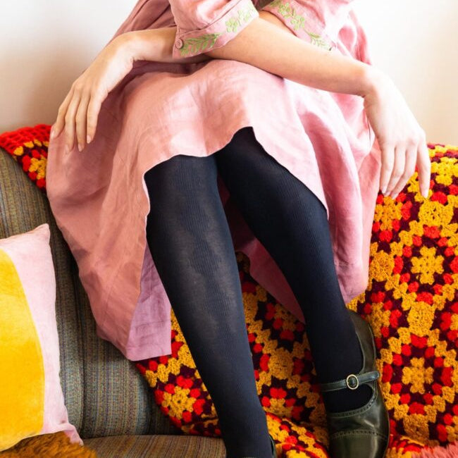 Person wearing black tights sitting on a colorful couch with a pink garment.