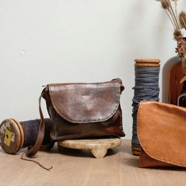 Brown leather bag on a wooden surface with spools of thread and a vase in the background.