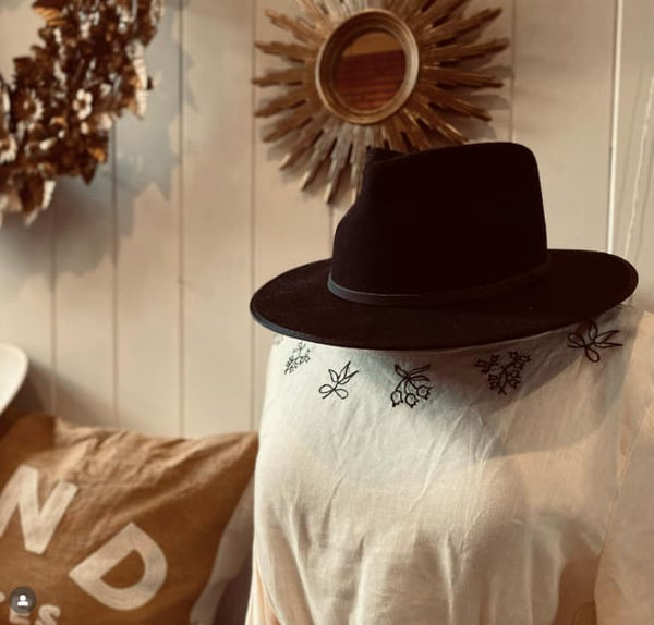 Person wearing a black hat and white shirt with embroidery in a rustic setting