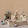 A styled nursery scene with two plush toy Maileg mice sitting on cream woven storage boxes, alongside miniature furniture and decor including a small teal watering can, stool, and heart-shaped cushion against a beige textured wall.