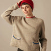 Person wearing a beige  Eribe Tweed Nep wool sweater with blue accents and a red knit beanie against a neutral background