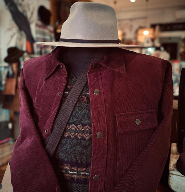 Mannequin wearing a maroon jacket, patterned sweater, and beige fedora in a store setting.