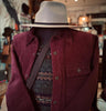 Mannequin wearing a maroon jacket, patterned sweater, and beige fedora in a store setting.