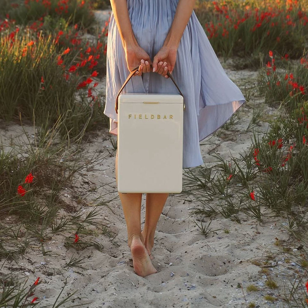 Person holding a beige 'FIELDBAR' cooler in a field of red flowers