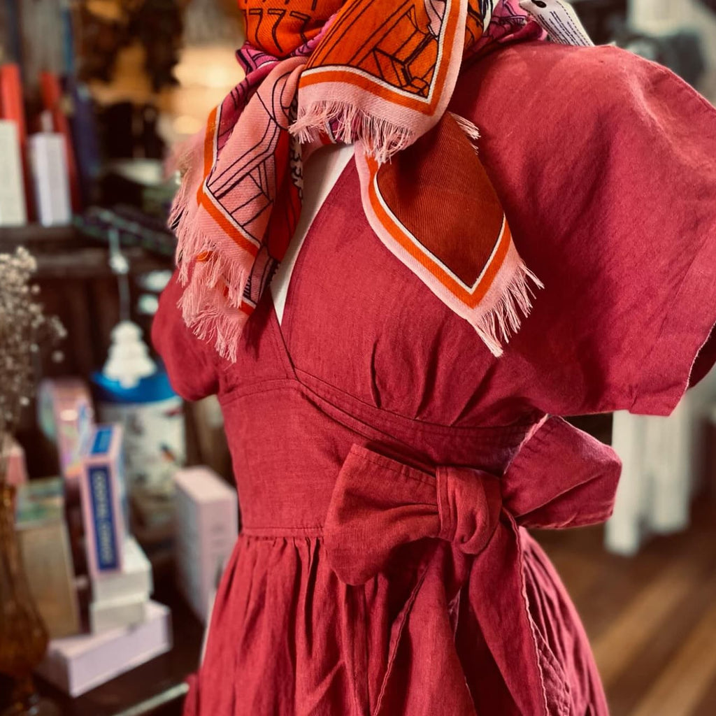Person wearing a red dress with an orange and pink patterned scarf in a store setting
