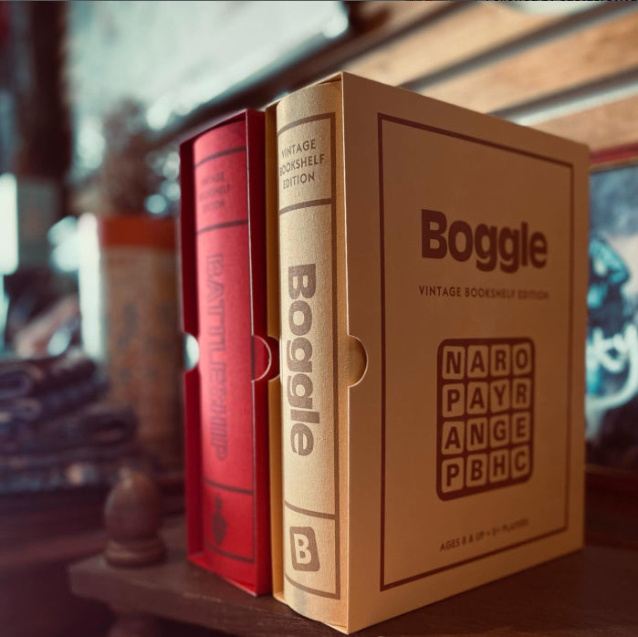 Two vintage bookshelf games 'Boggle' + 'Battleship' board game boxes on a shelf with a blurred background
