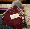 Maroon knit beanie with gray pom-pom and 'Tightology' label dotty socks on a textured fabric background