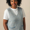 Woman wearing a gray knitted vest over a white shirt against a beige background
