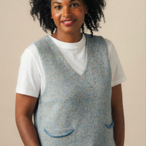 Woman wearing a gray knitted vest over a white shirt against a beige background