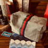 Khaki toiletry bag with red and green stripe on a wooden surface with grooming products.