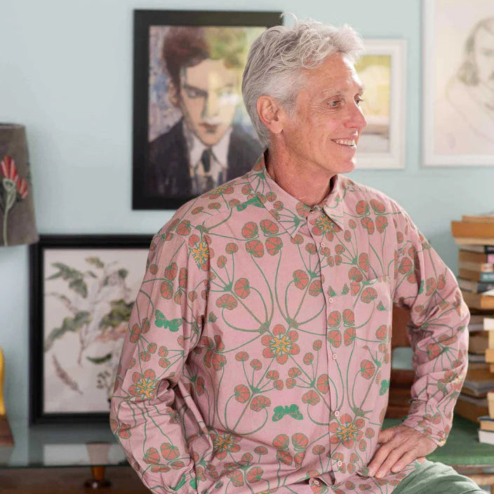 Man wearing a pink floral shirt sitting in a room with light blue walls and framed pictures.
