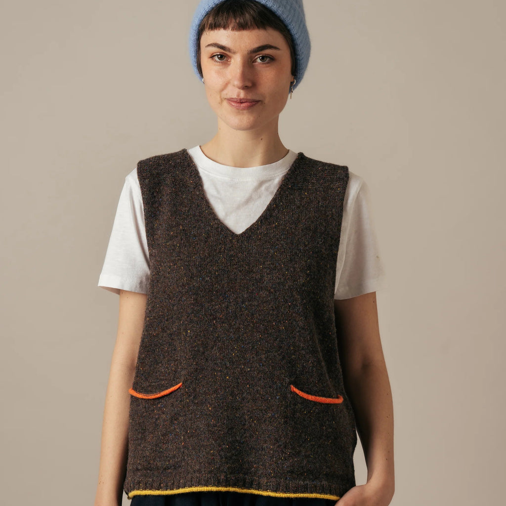 Person wearing a brown sleeveless woolen Eribe Tweed Nep Vest over a white shirt with a blue knit cap on a beige background