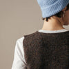 Person wearing a brown knitted vest over a white shirt with a blue knit hat on a neutral background