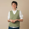 Person wearing a green knitted vest over a white shirt with blue pants on a beige background