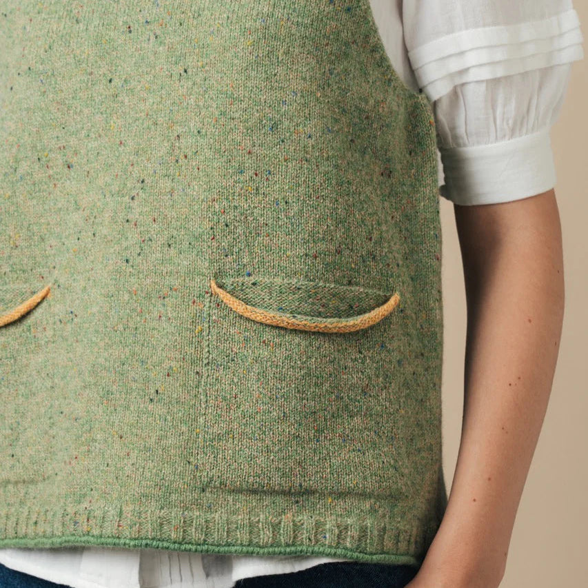 Green knitted vest with two front pockets worn over a white shirt and blue jeans.