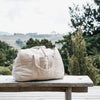 Beige duffel bag on a wooden bench with a scenic background