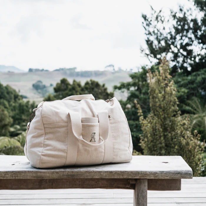 Beige duffel bag on a wooden bench with a scenic background