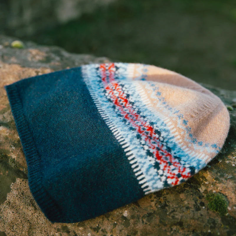 Knitted Eribe beanie with a colorful pattern on a stone surface
