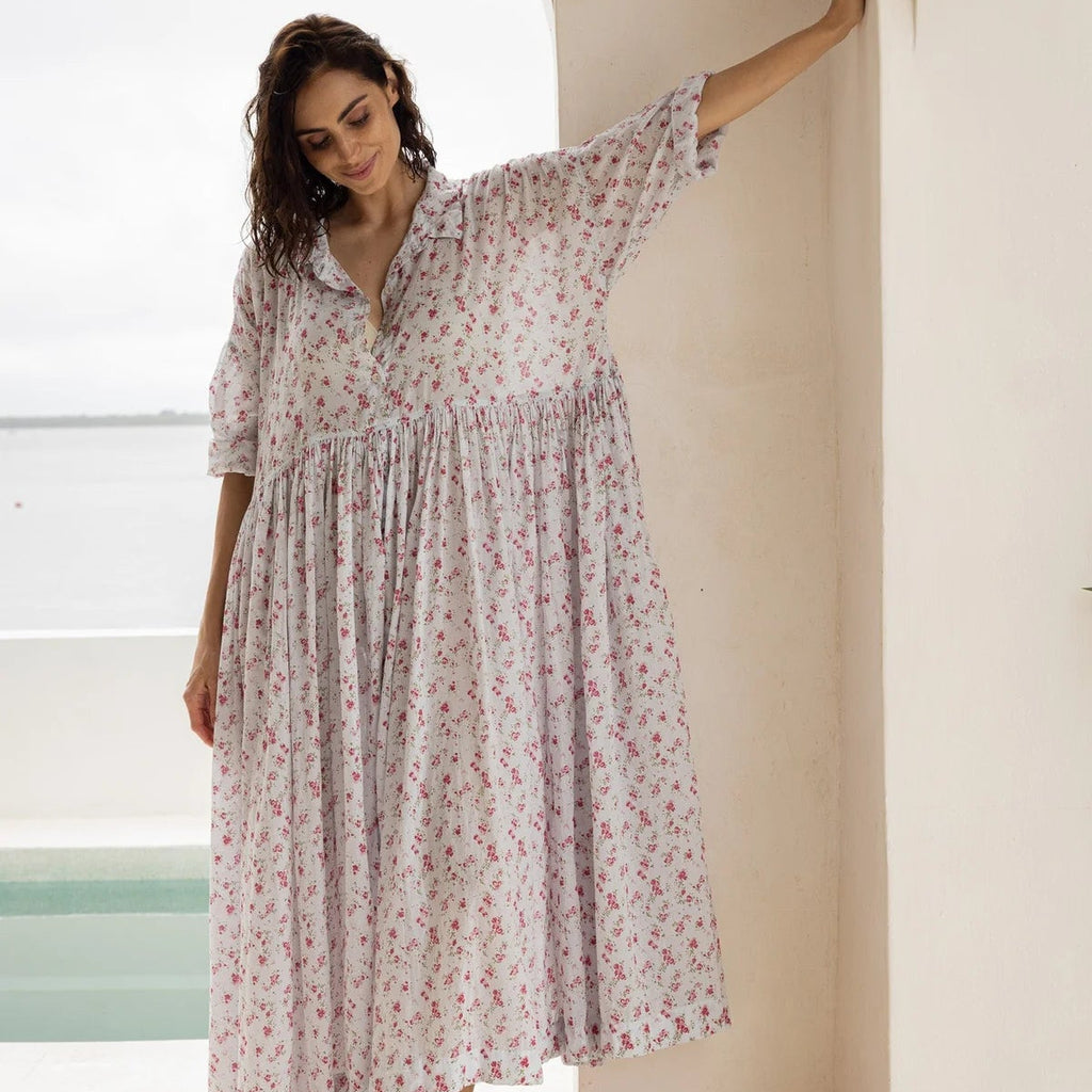 Woman in a floral dress standing in a bright room with large windows.