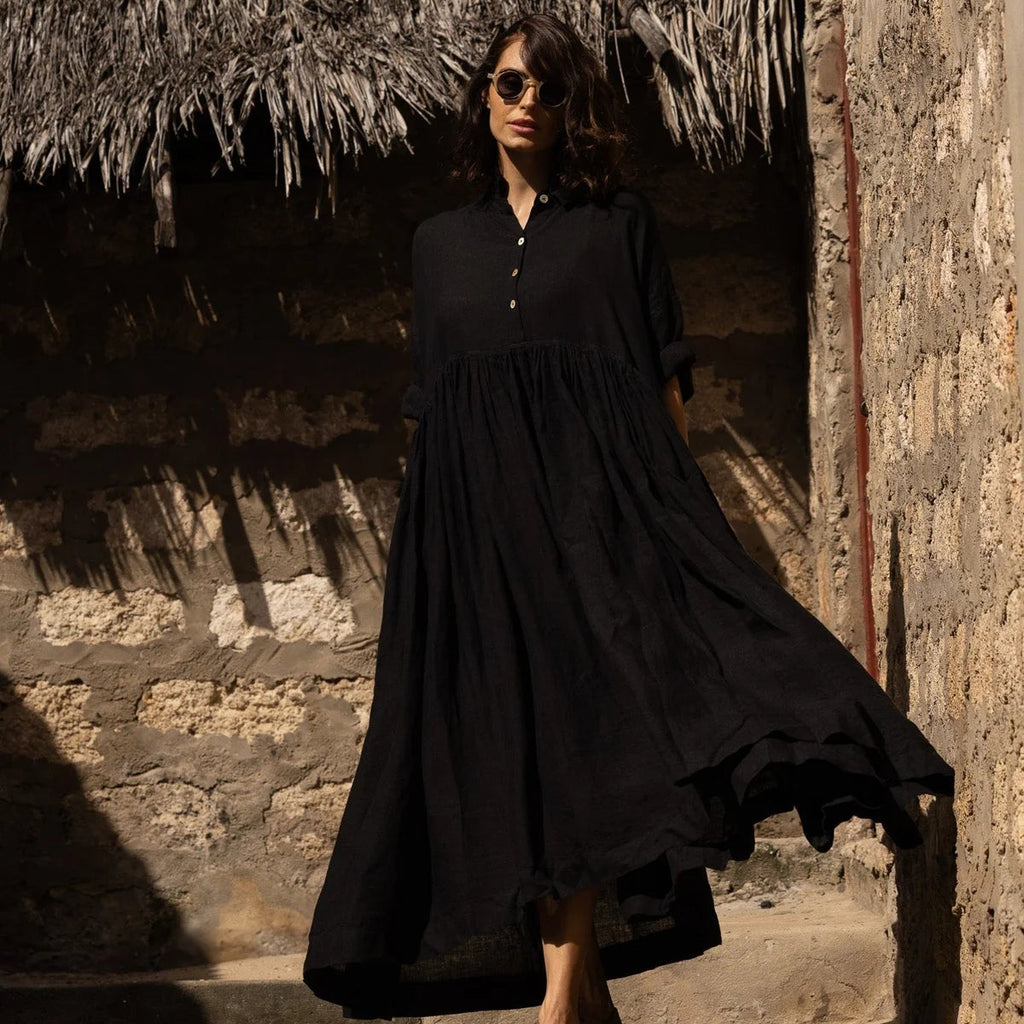 Woman in a black dress standing on stone steps with a rustic wall background